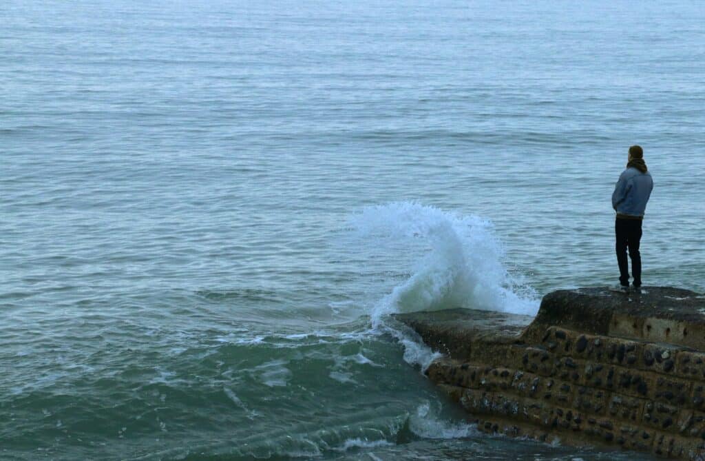 person standing on edge of cliff looking at ocean