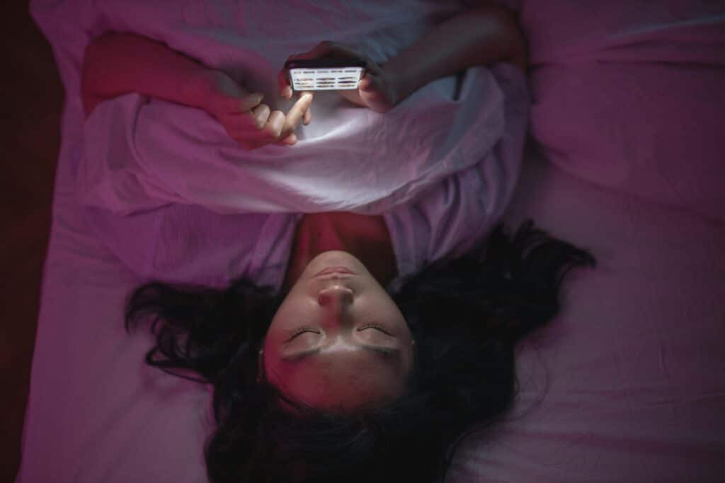 young woman laying in bed scrolling on phone