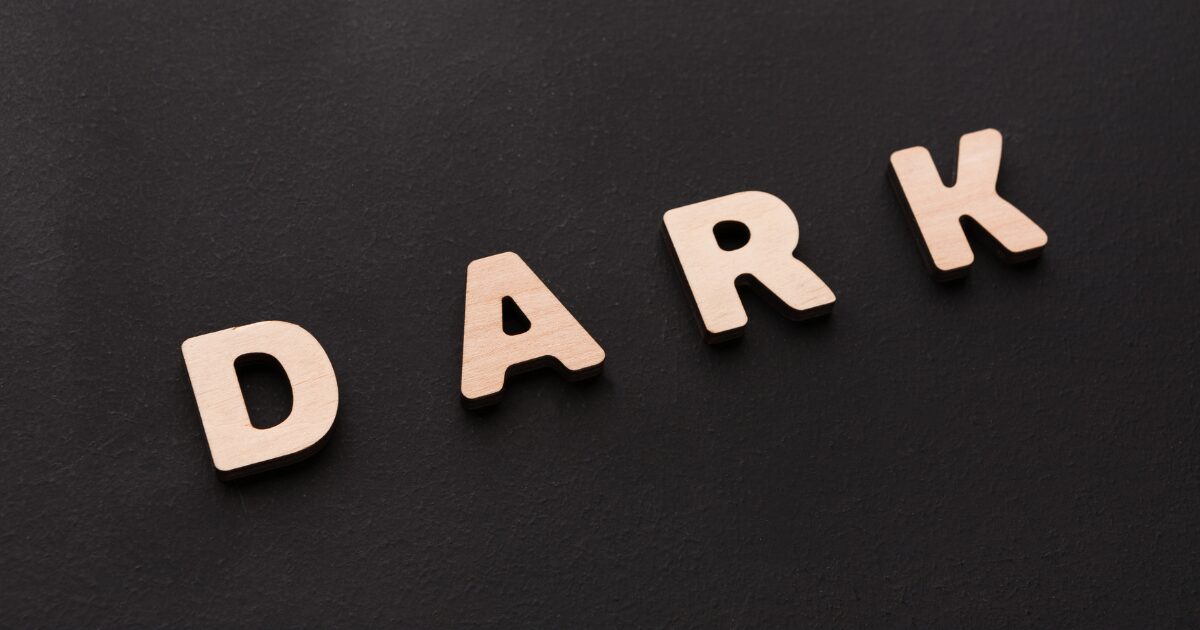 Wooden letters spell'DARK' on a black textured surface.