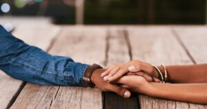 Two people hold hands resting on a rustic wooden table, conveying support and connection.