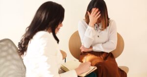 - Treat Mental Health Tennessee Therapist taking notes as a distressed client covers her face with her hand during a counseling session.