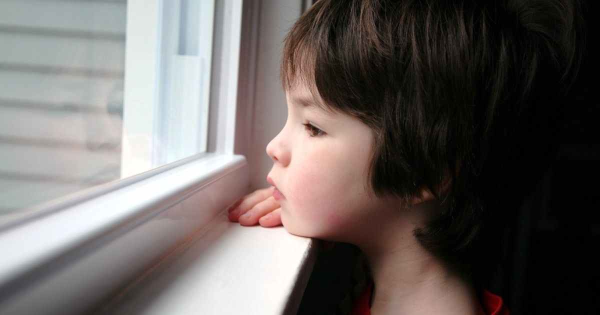 Child gazing out a window, resting hands on the sill, lost in thought.