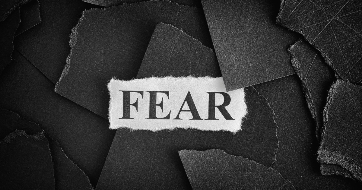 Piece of torn white paper with the bold word FEAR, laid on dark, layered torn fragments for a stark, ominous effect.