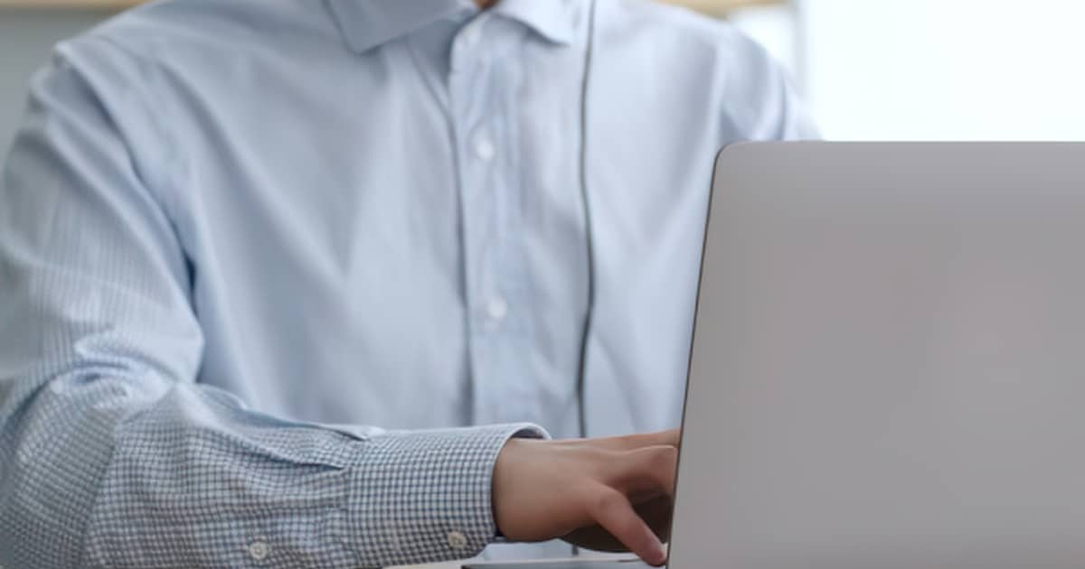 Person wearing a light blue shirt typing on a laptop at a desk.